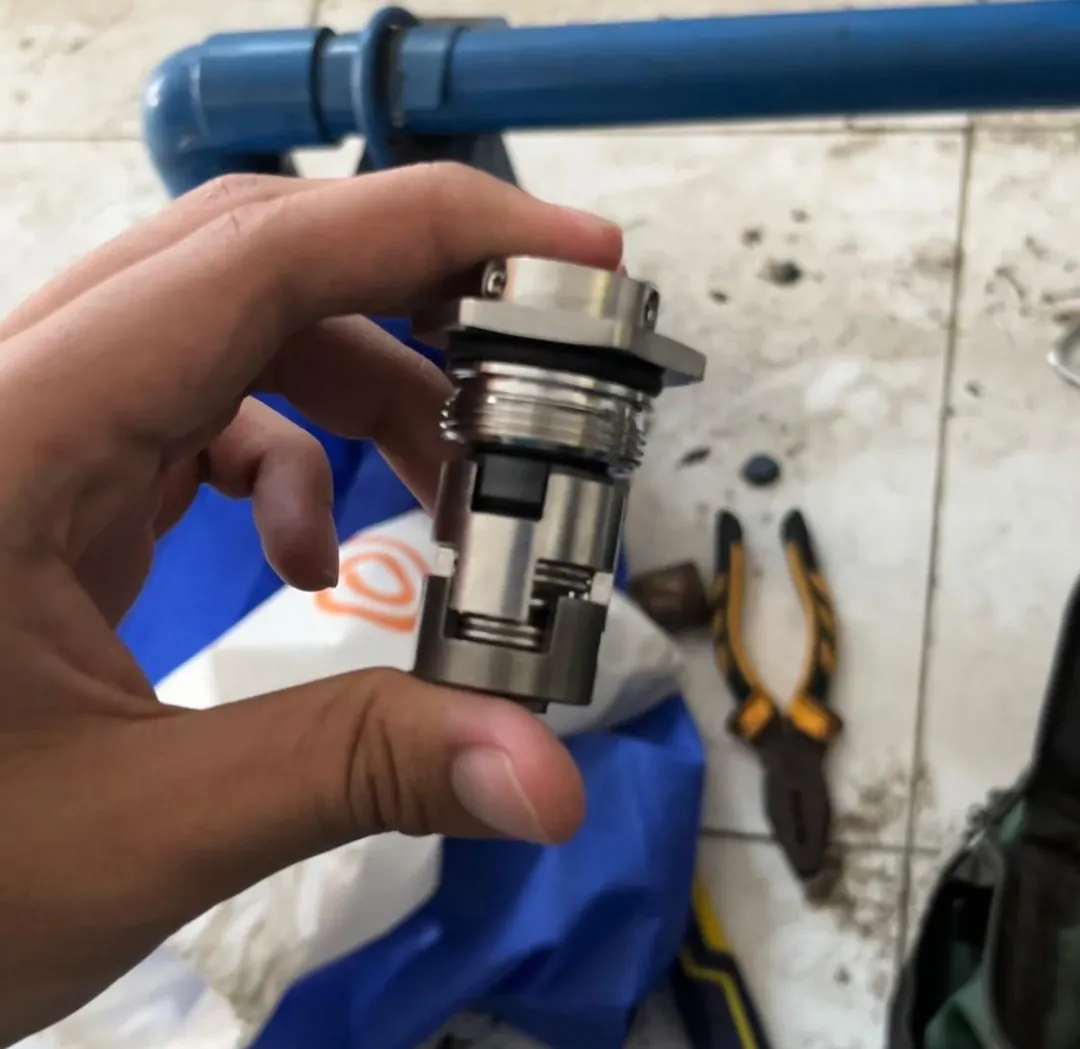 Komponen seal pompa air yang dipegang tangan, dengan tang dan perlengkapan kerja di lantai